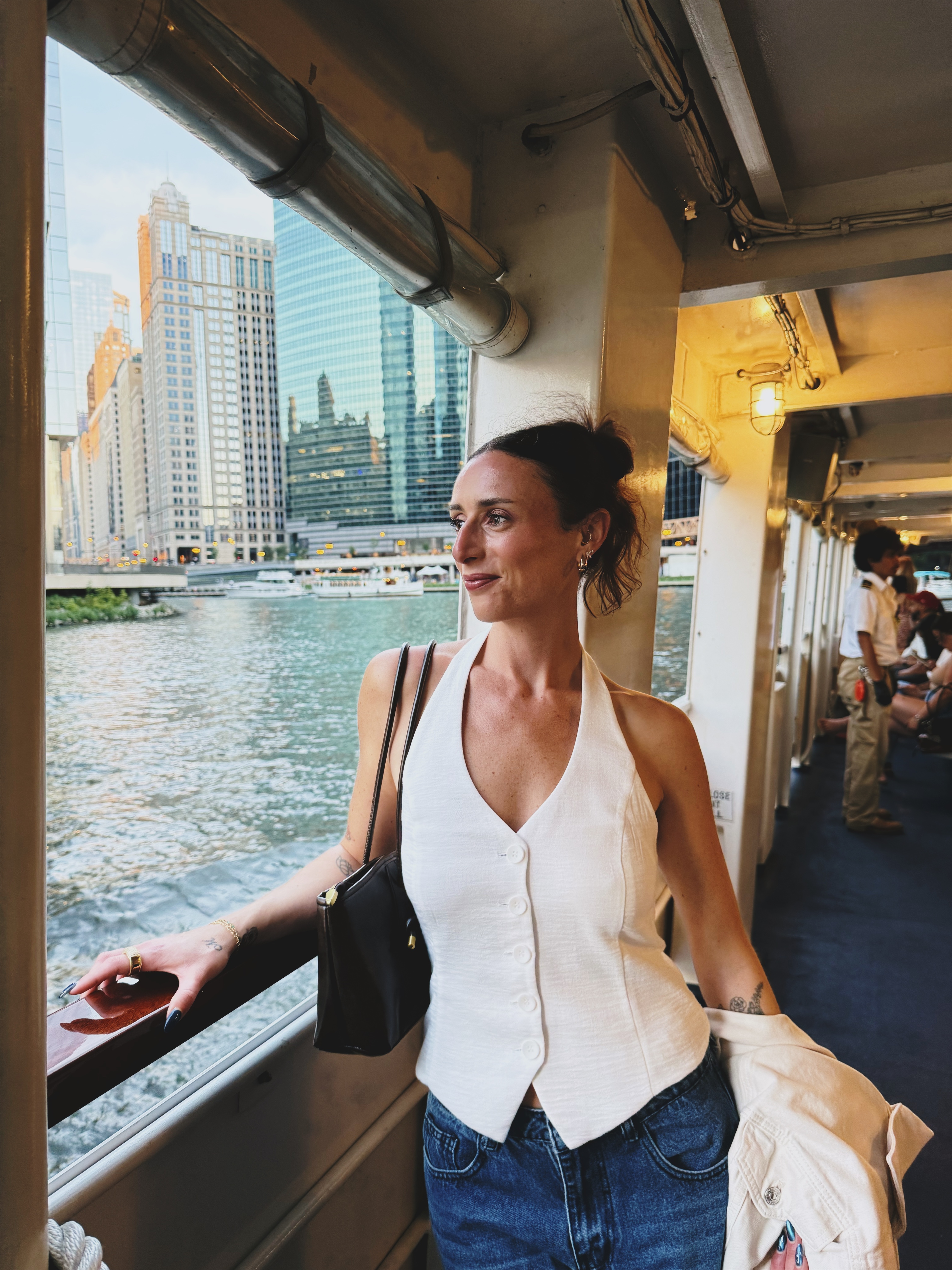 Jenna Kronyak on a river boat in a white halter top, looking out at the Chicago skyline in late afternoon light.